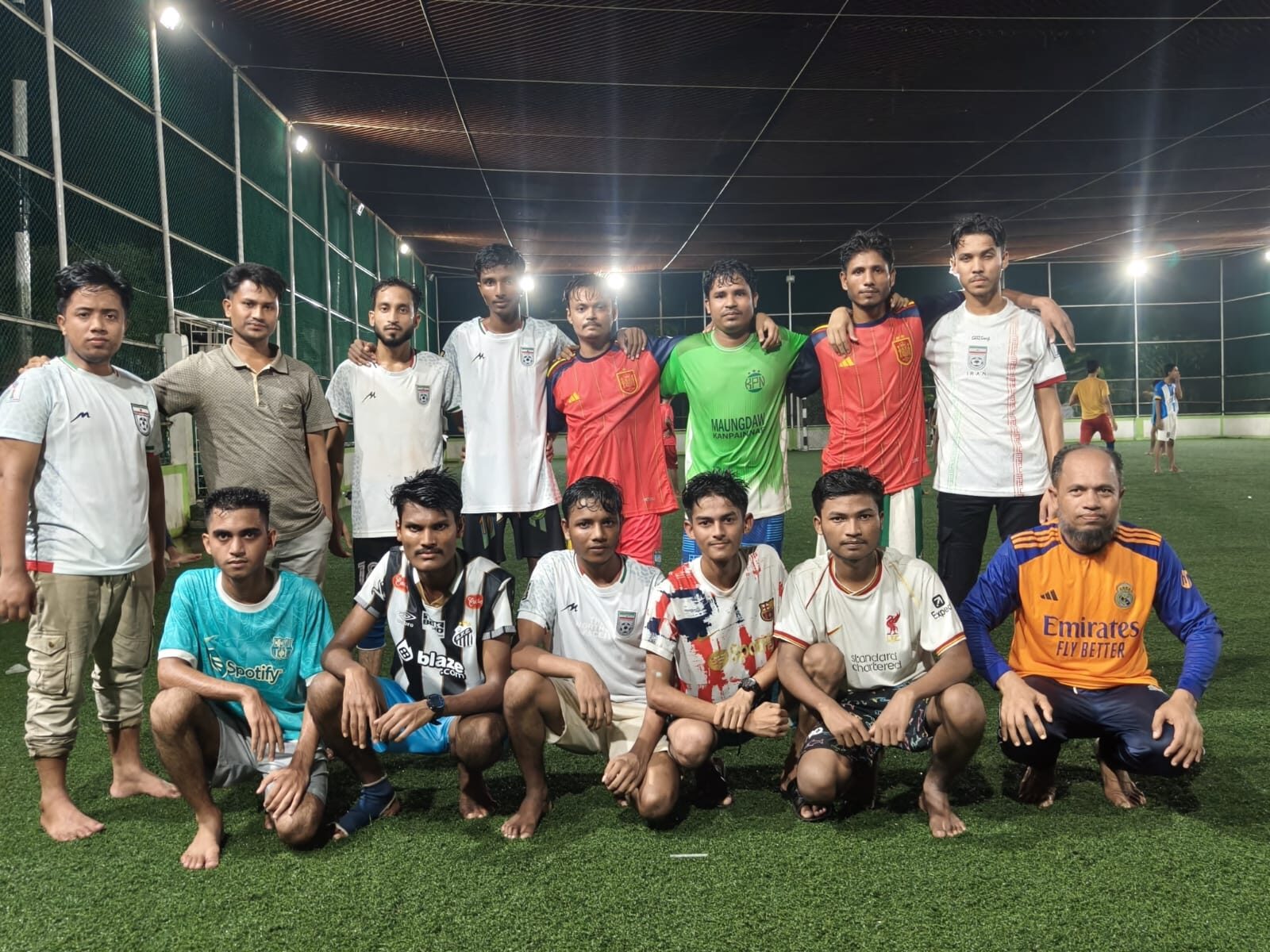 Staff football team lined up on a floodlit artificial pitch at night