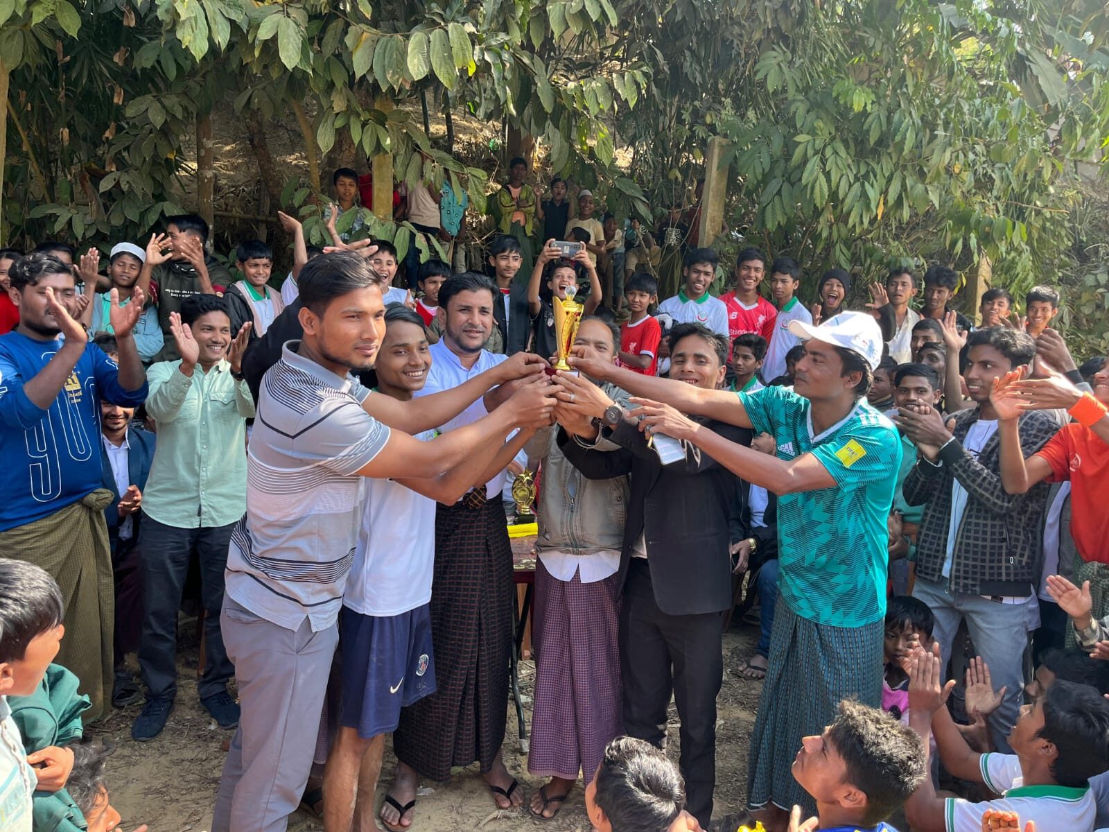 Organisers and team captains holding the tournament trophy together as a crowd applauds