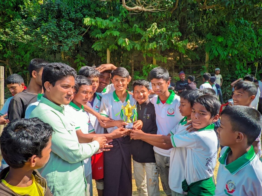 A teacher handing the trophy to students in green and white school kit