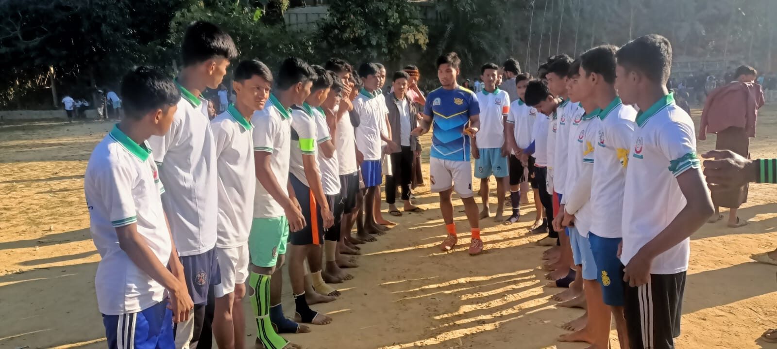 Two teams standing in facing lines across the pitch before a match