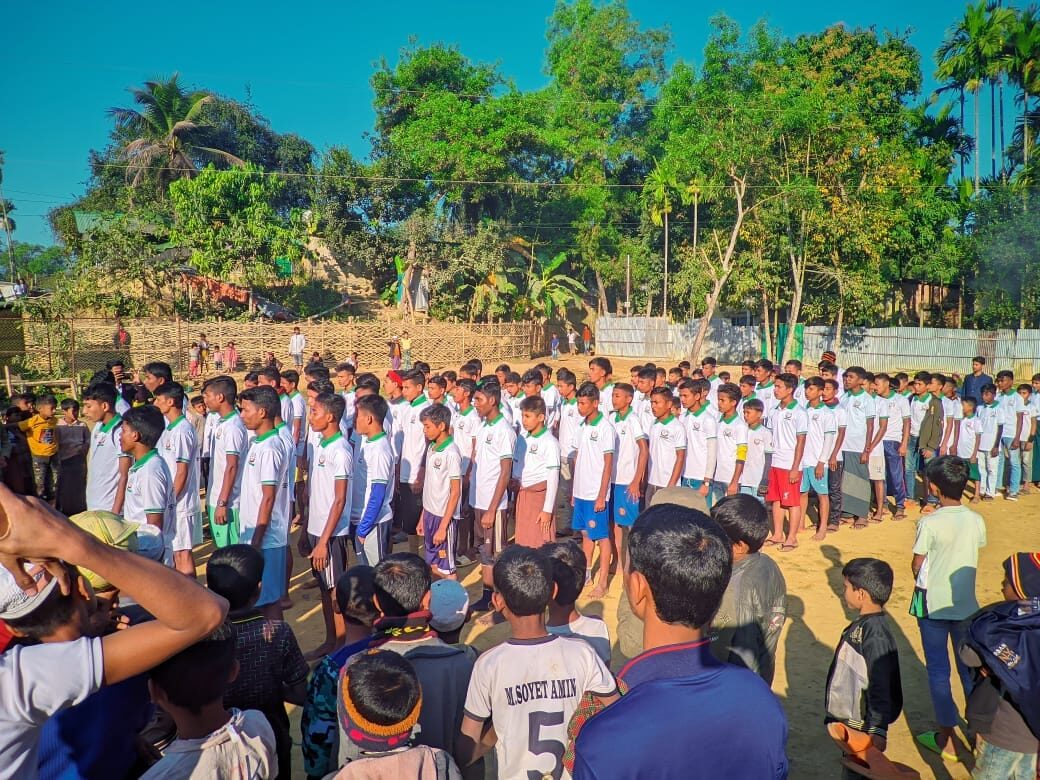 Rows of students in school kit standing to attention while a crowd watches