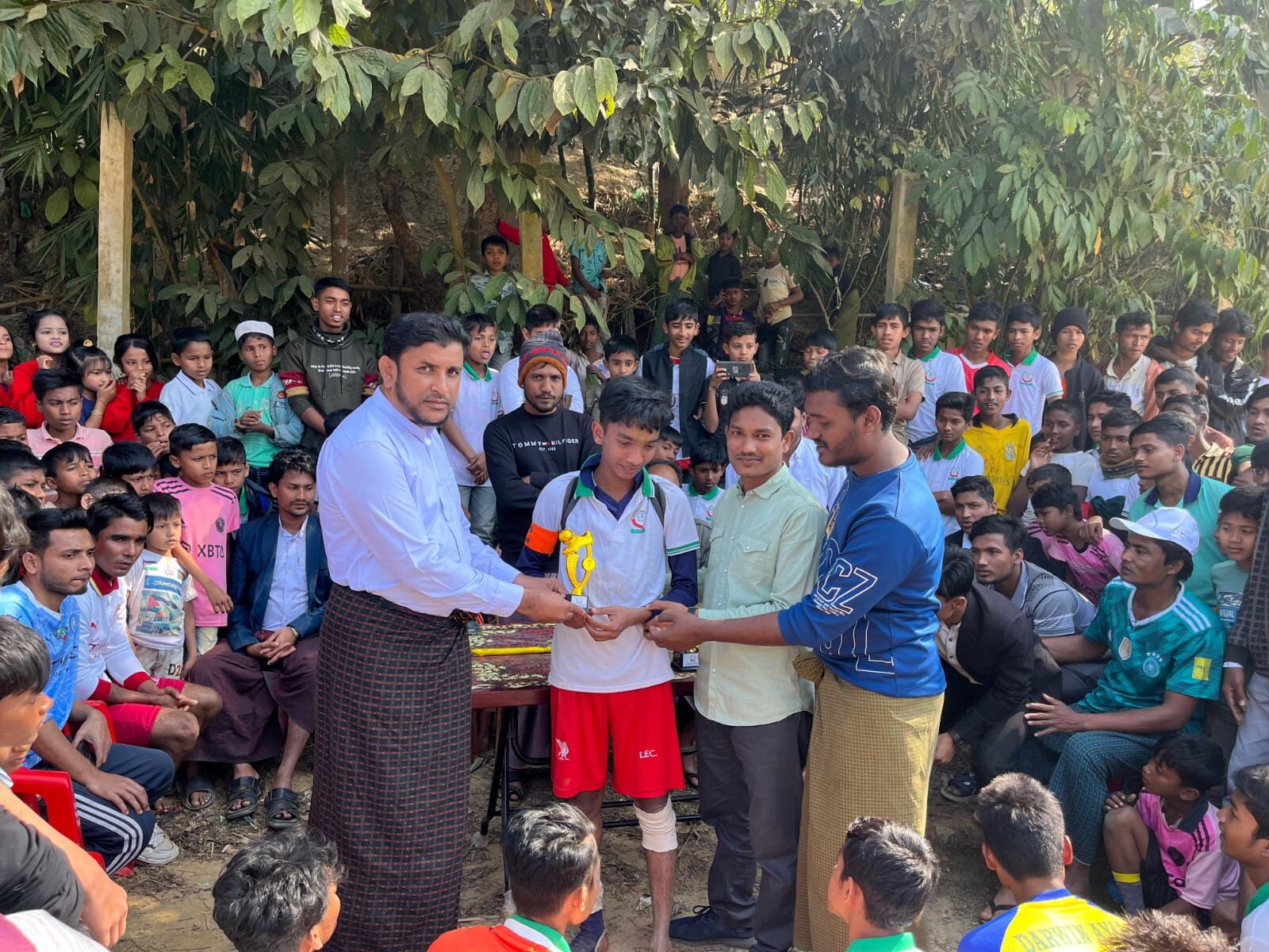 A school official presenting a small trophy to a student player in front of a seated crowd