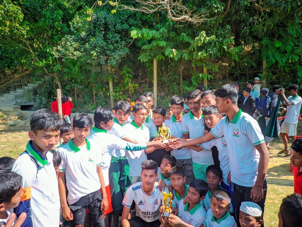 Students in school kit crowded together holding a trophy up between them